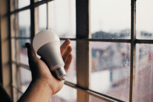 A hand holding an energy efficient light bulb in front of a window.