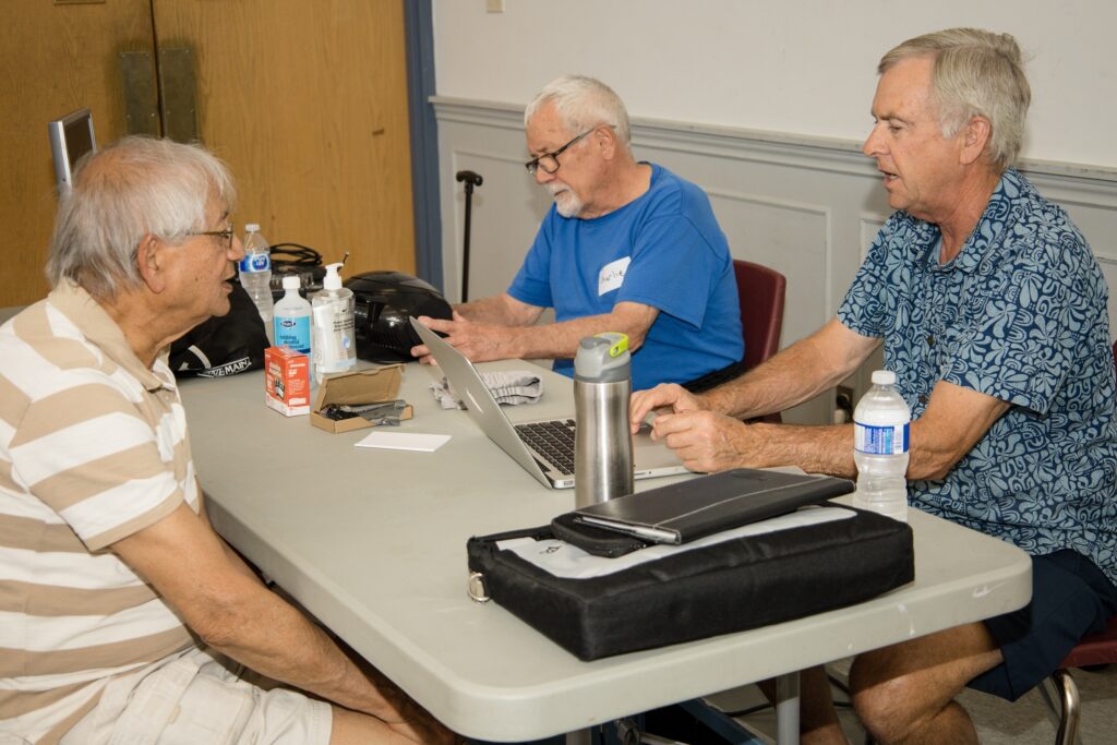 A photo of three men sitting at a table at the Repair Cafe. One man is working on a computer.