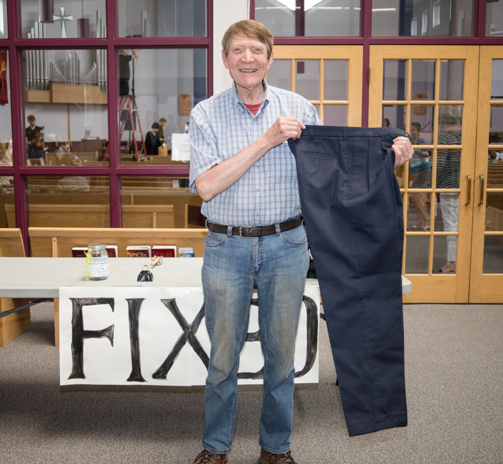 photograph of a man holding up a pair of blue pants that were repaired at the 2024 repair cafe
